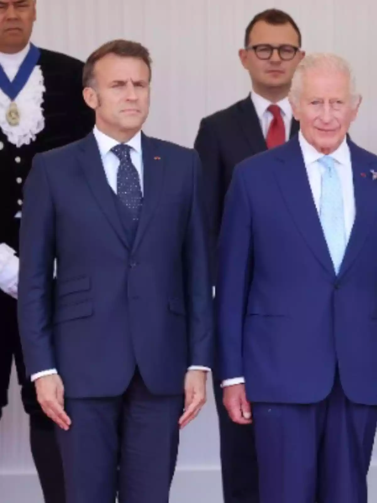 Two men in blue suits pose together at a formal event, accompanied by other people in the background.