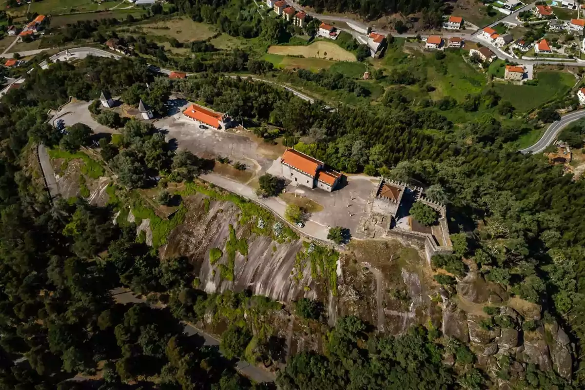 Vista aérea de un castillo y varios edificios con techos rojos rodeados de árboles y vegetación en una zona montañosa