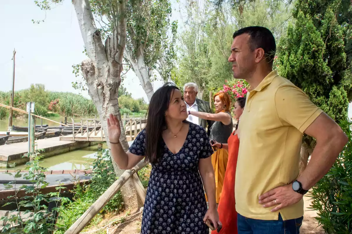 Varias personas conversan al aire libre junto a un embarcadero rodeado de árboles y vegetación