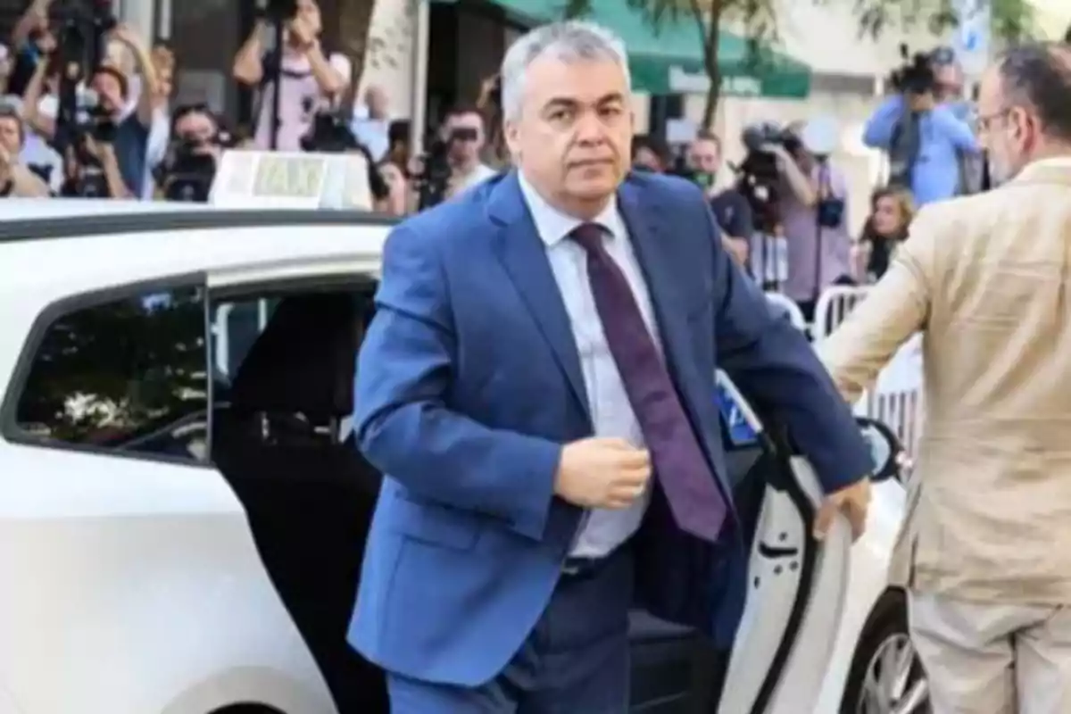 Hombre de traje azul saliendo de un taxi blanco mientras varias personas y fotógrafos lo observan al fondo Hombre de traje azul saliendo de un taxi blanco mientras varias personas y fotógrafos lo observan al fondo