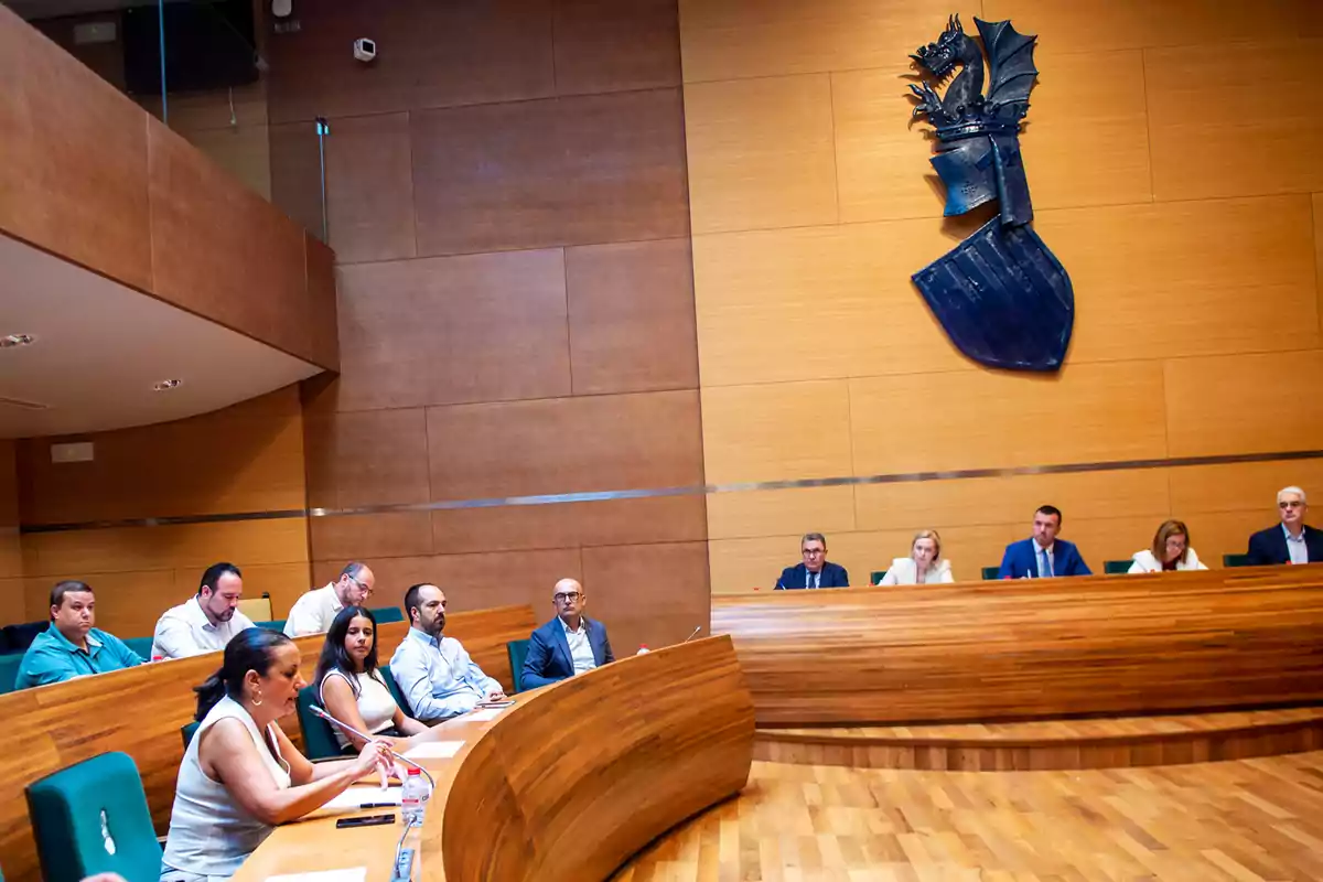 Personas sentadas en una sala de reuniones de madera con un escudo de dragón en la pared Personas sentadas en una sala de reuniones de madera con un escudo de dragón en la pared