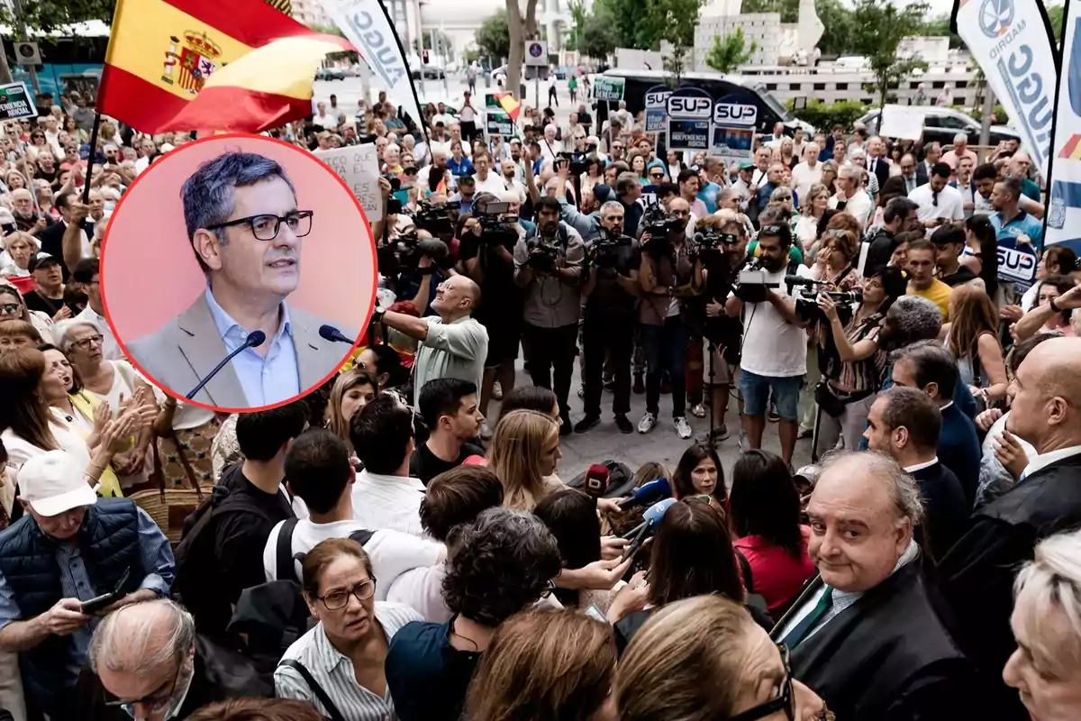 Una multitud de personas se manifiesta en la calle con banderas y pancartas mientras un recuadro muestra a un hombre con gafas hablando frente a micrófonos.