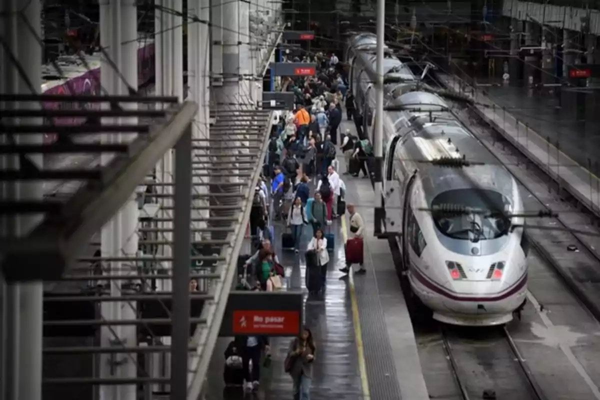 Personas caminando y esperando junto a un tren de alta velocidad en una estación concurrida