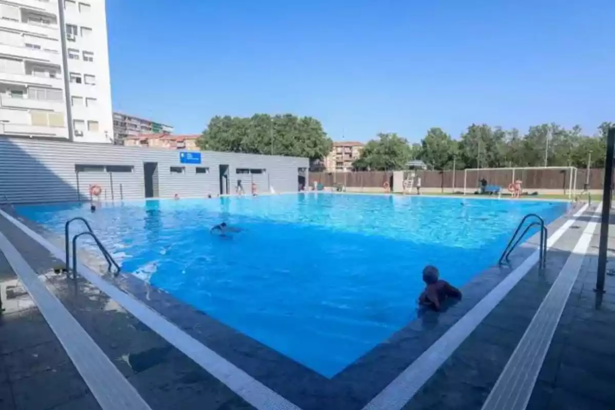 Piscina al aire libre en una zona urbana con varias personas disfrutando del agua en un día soleado