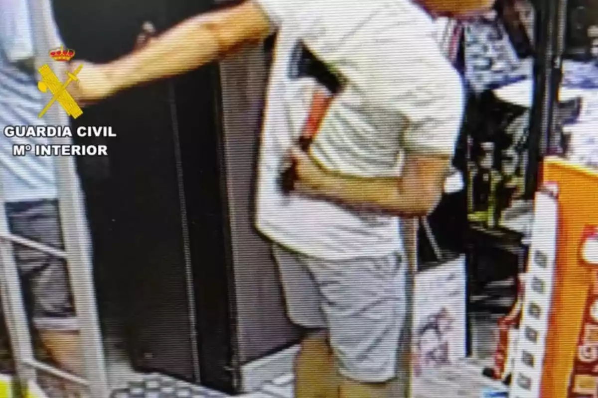 Persona con camiseta clara y pantalón corto sosteniendo un hacha dentro de una tienda con el logo de la Guardia Civil en la esquina superior izquierda