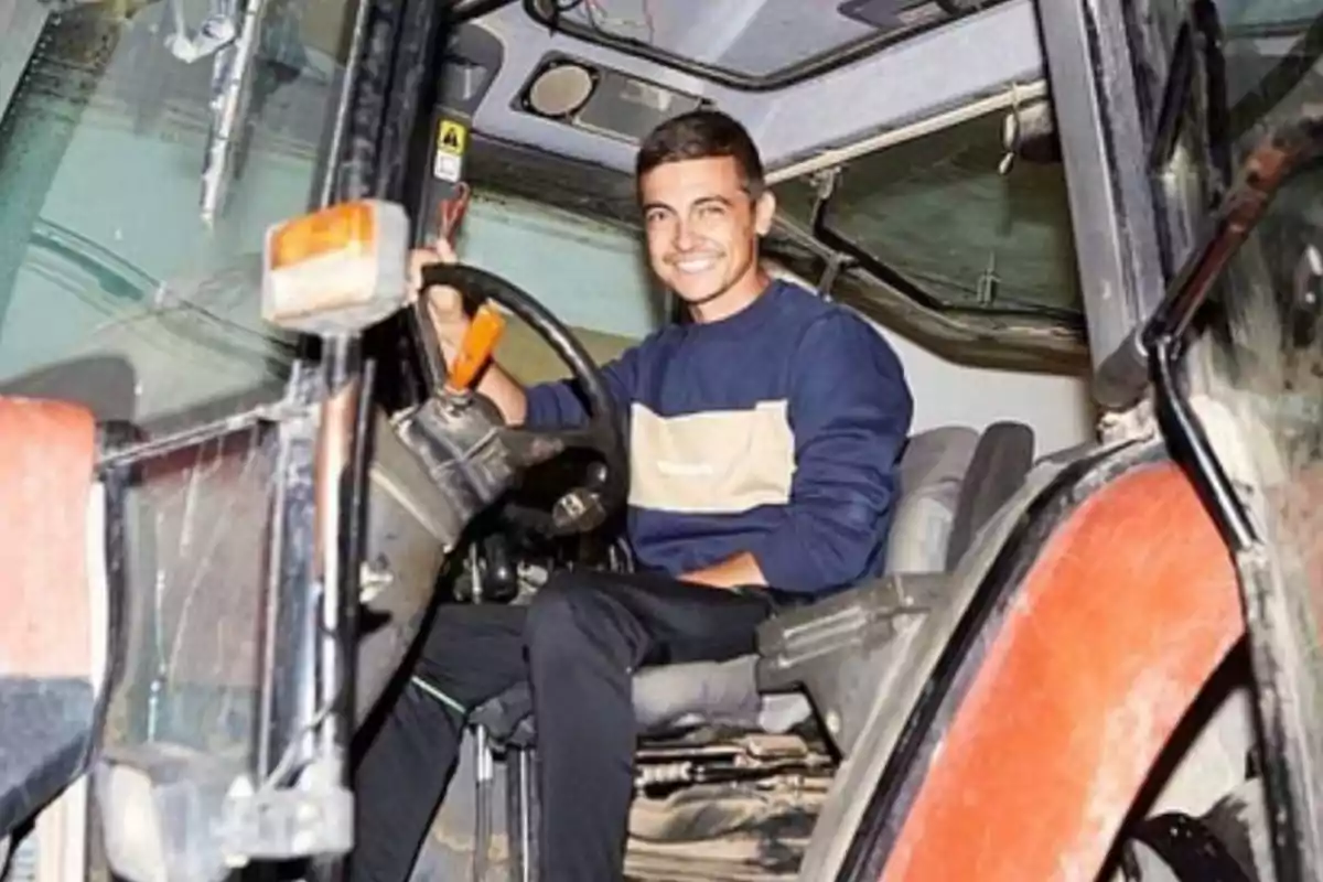 Joven sonriente sentado al volante de un tractor dentro de la cabina