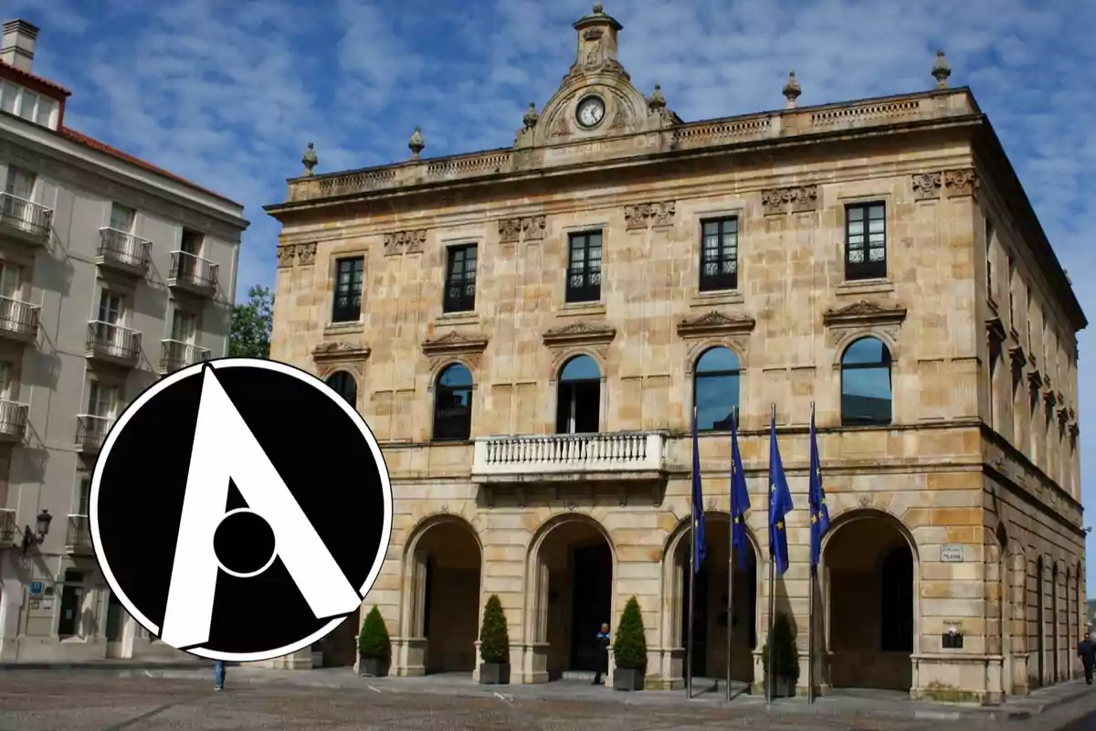 Fachada de un edificio histórico con varias banderas azules al frente y un gran logotipo circular en blanco y negro en la esquina inferior izquierda
