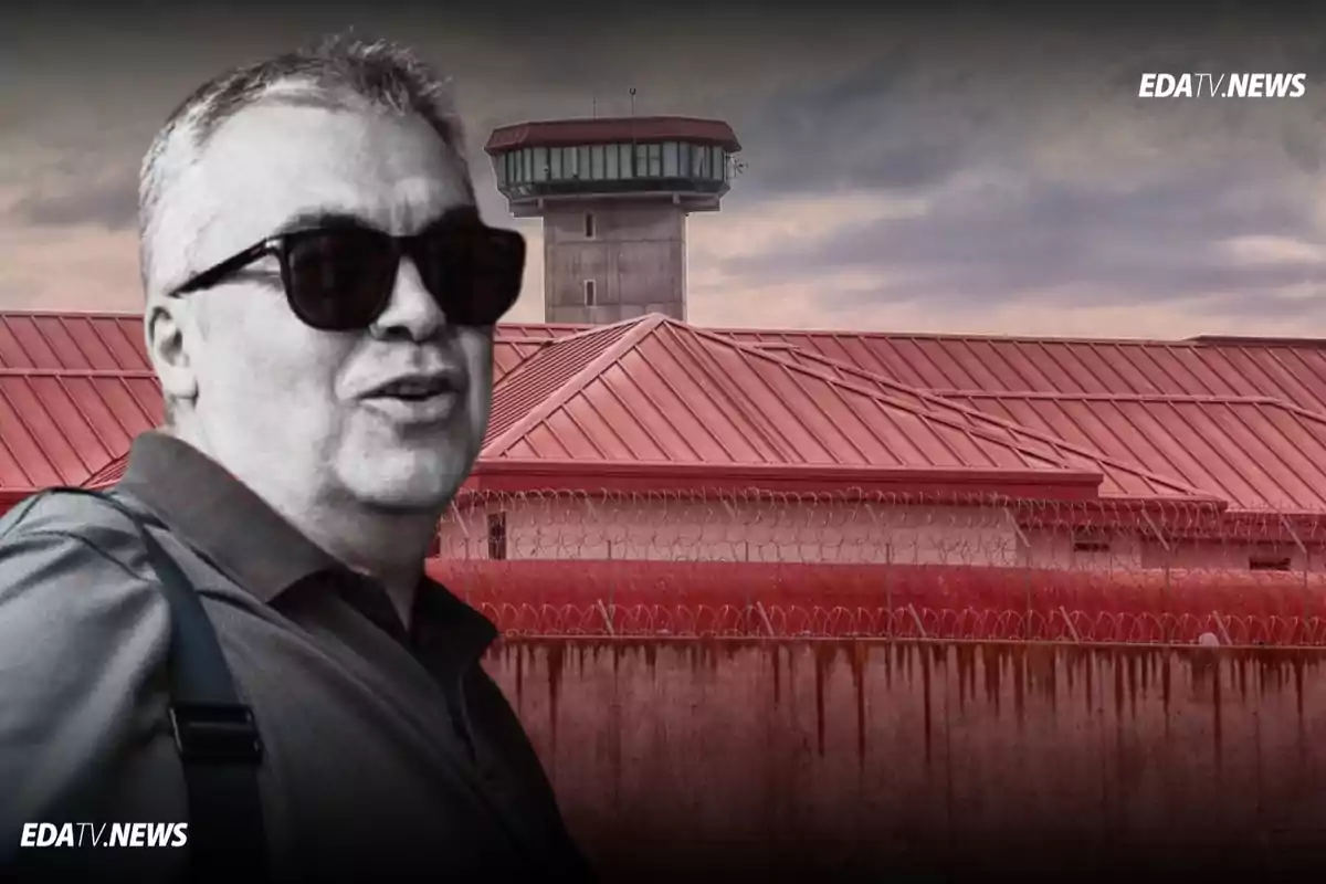 Hombre con gafas oscuras en primer plano frente a una prisión con alambre de púas y torre de vigilancia al fondo