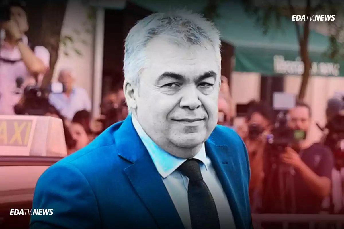 Hombre de cabello canoso con traje azul y corbata negra sonriendo mientras camina frente a un grupo de personas y cámaras de prensa