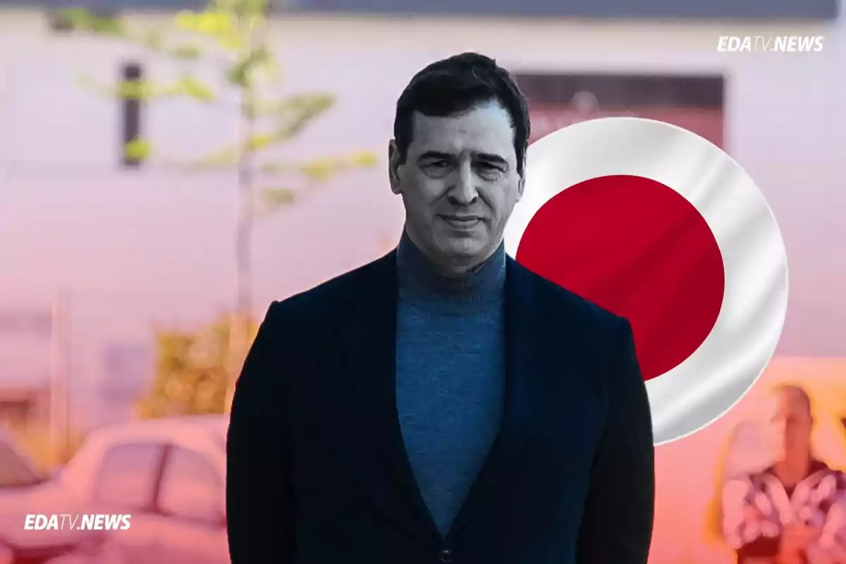 Hombre de cabello oscuro con suéter gris y saco negro de pie frente a una bandera de Japón y un fondo urbano desenfocado