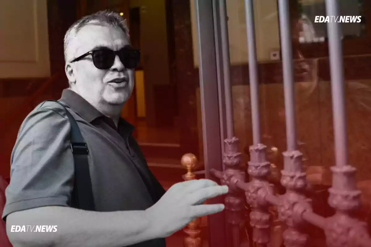 Hombre con gafas de sol y camisa oscura abriendo una puerta de metal mientras mira hacia la cámara