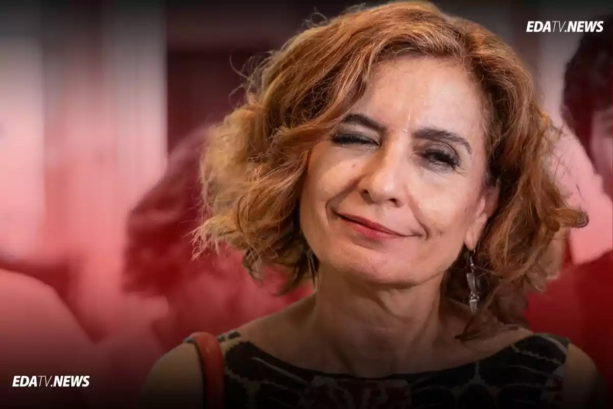 Mujer de cabello rizado y pelirrojo guiñando un ojo y sonriendo levemente frente a un fondo desenfocado