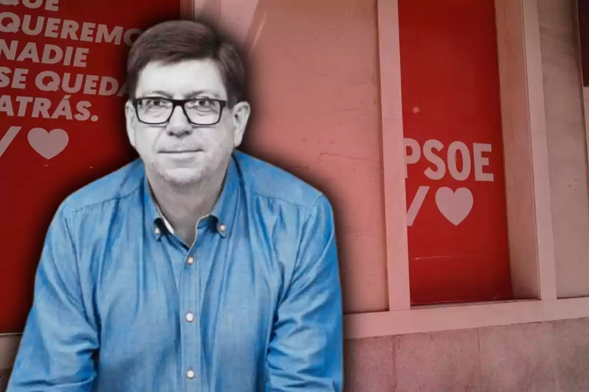 Hombre con gafas y camisa azul frente a una pared con carteles rojos del PSOE y mensajes en letras blancas