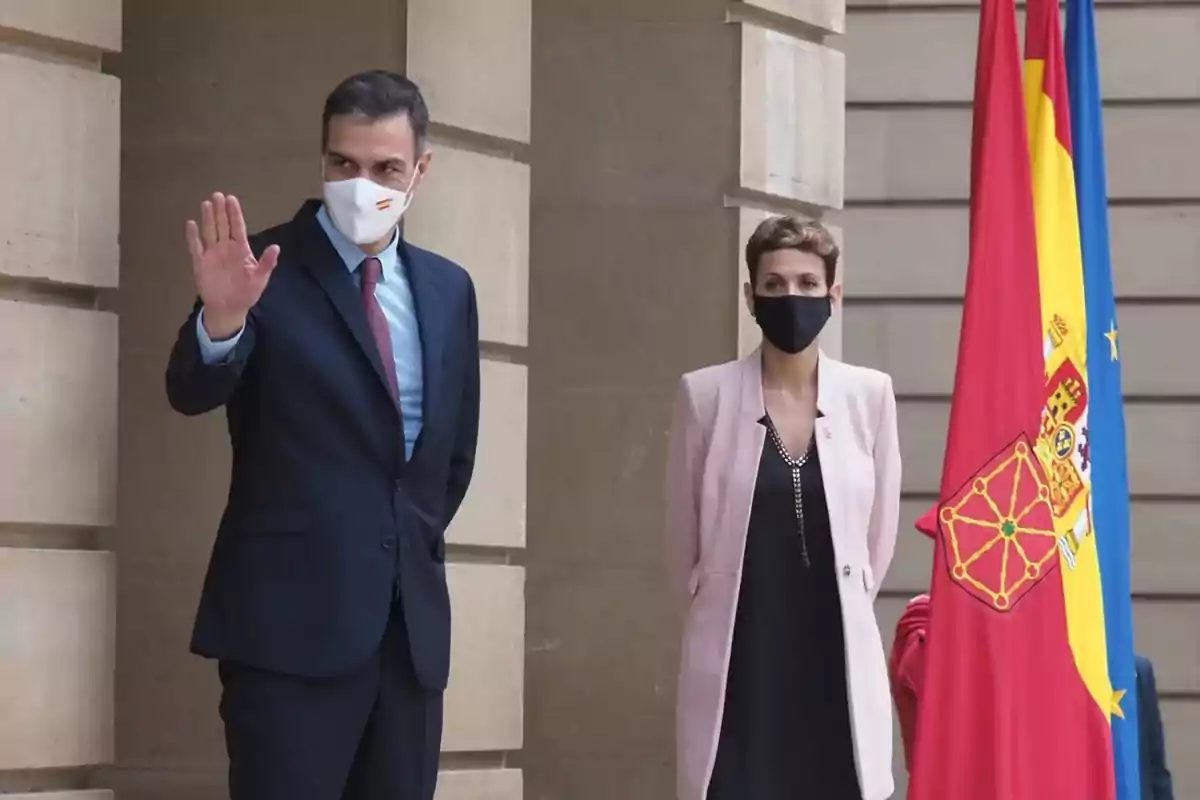 Dos personas con mascarilla de pie junto a banderas de España y la Unión Europea en un entorno institucional Dos personas con mascarilla de pie junto a banderas de España y la Unión Europea en un entorno institucional