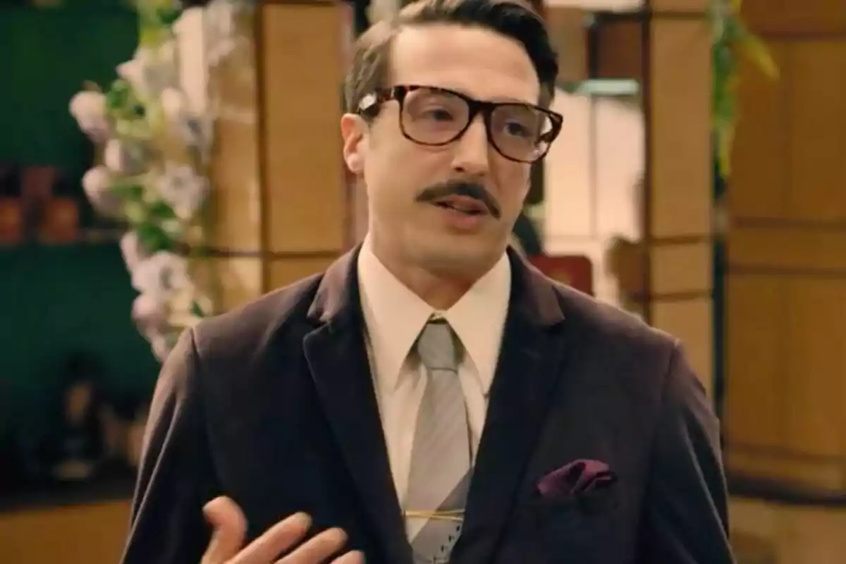 Cobeaga con gafas grandes y bigote vestido con traje oscuro y corbata clara en un ambiente interior elegante. Cobeaga con gafas grandes y bigote vestido con traje oscuro y corbata clara en un ambiente interior elegante.
