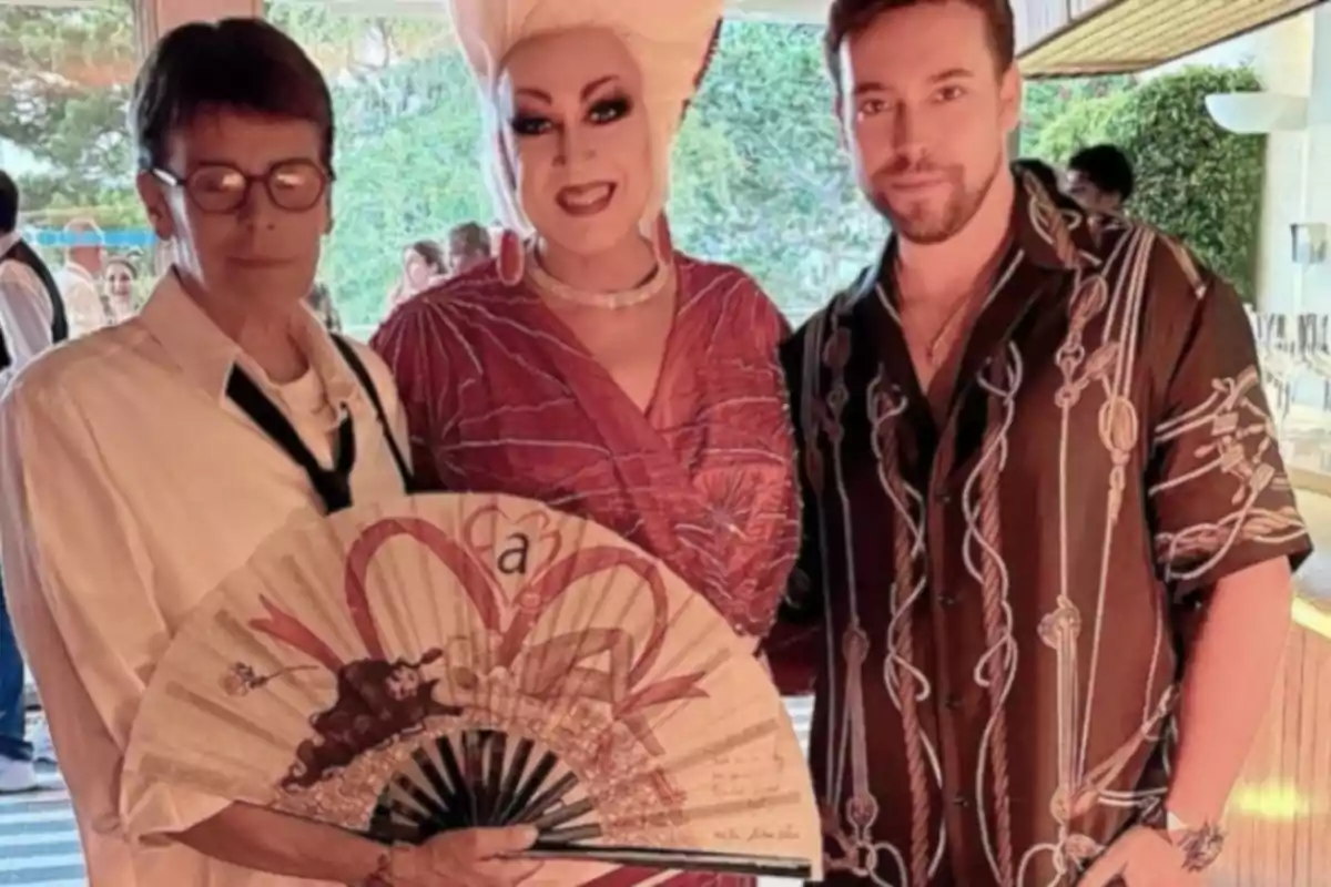 Tres personas posan juntas en un evento social, una de ellas sostiene un abanico decorado y otra lleva un elaborado peinado y maquillaje llamativo Tres personas posan juntas en un evento social, una de ellas sostiene un abanico decorado y otra lleva un elaborado peinado y maquillaje llamativo