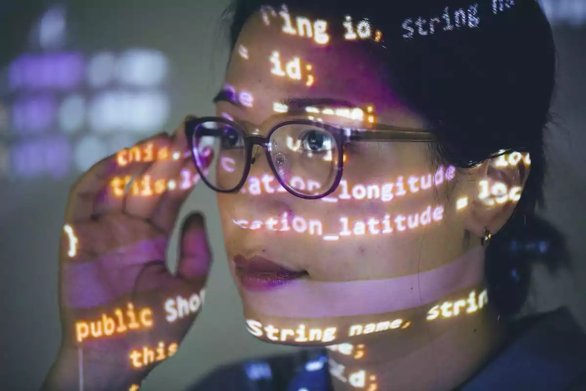 Mujer con gafas observando atentamente mientras líneas de código se proyectan sobre su rostro