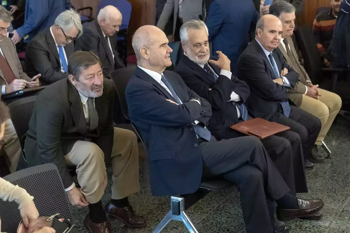 Varios hombres vestidos de traje y corbata están sentados en una sala, algunos con los brazos cruzados y otros en actitud pensativa, mientras esperan el inicio de un evento o reunión. Varios hombres vestidos de traje y corbata están sentados en una sala, algunos con los brazos cruzados y otros en actitud pensativa, mientras esperan el inicio de un evento o reunión.