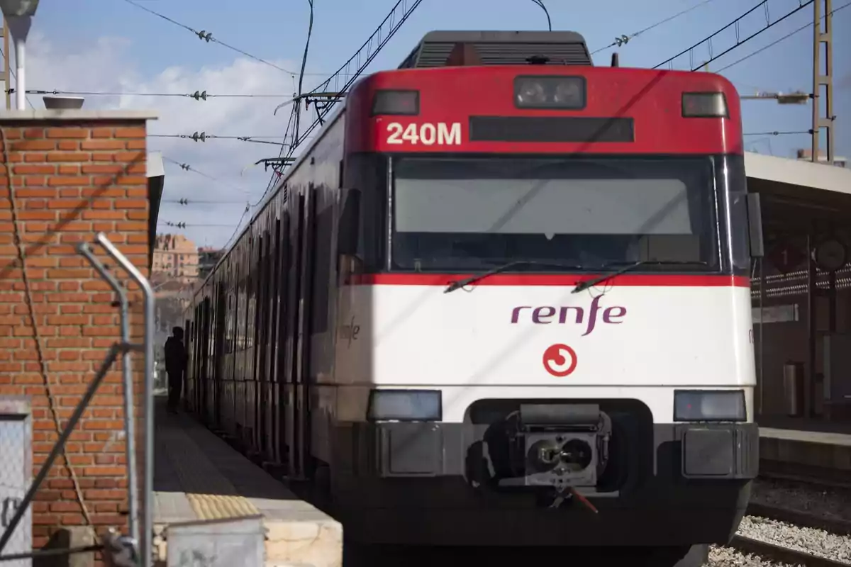 Tren de cercanías de Renfe detenido en una estación con una persona esperando en el andén Tren de cercanías de Renfe detenido en una estación con una persona esperando en el andén