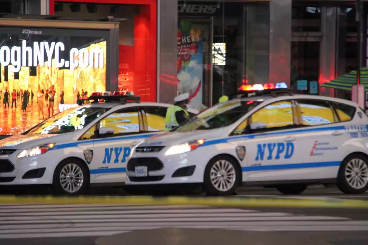 Dos patrullas de la policía de Nueva York con las luces encendidas están estacionadas en una calle junto a un cruce peatonal