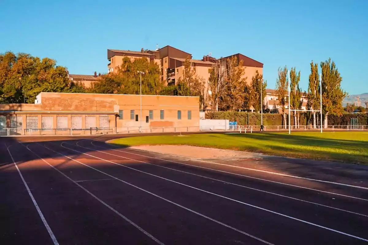Pista de atletismo al aire libre junto a un edificio de ladrillo y árboles en un día soleado Pista de atletismo al aire libre junto a un edificio de ladrillo y árboles en un día soleado