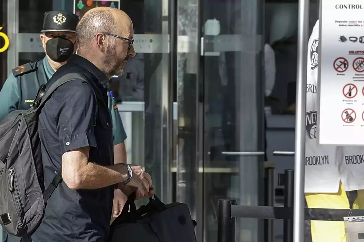 Un hombre con mochila y maletín pasa por un control de seguridad mientras un guardia civil lo observa en el fondo Un hombre con mochila y maletín pasa por un control de seguridad mientras un guardia civil lo observa en el fondo