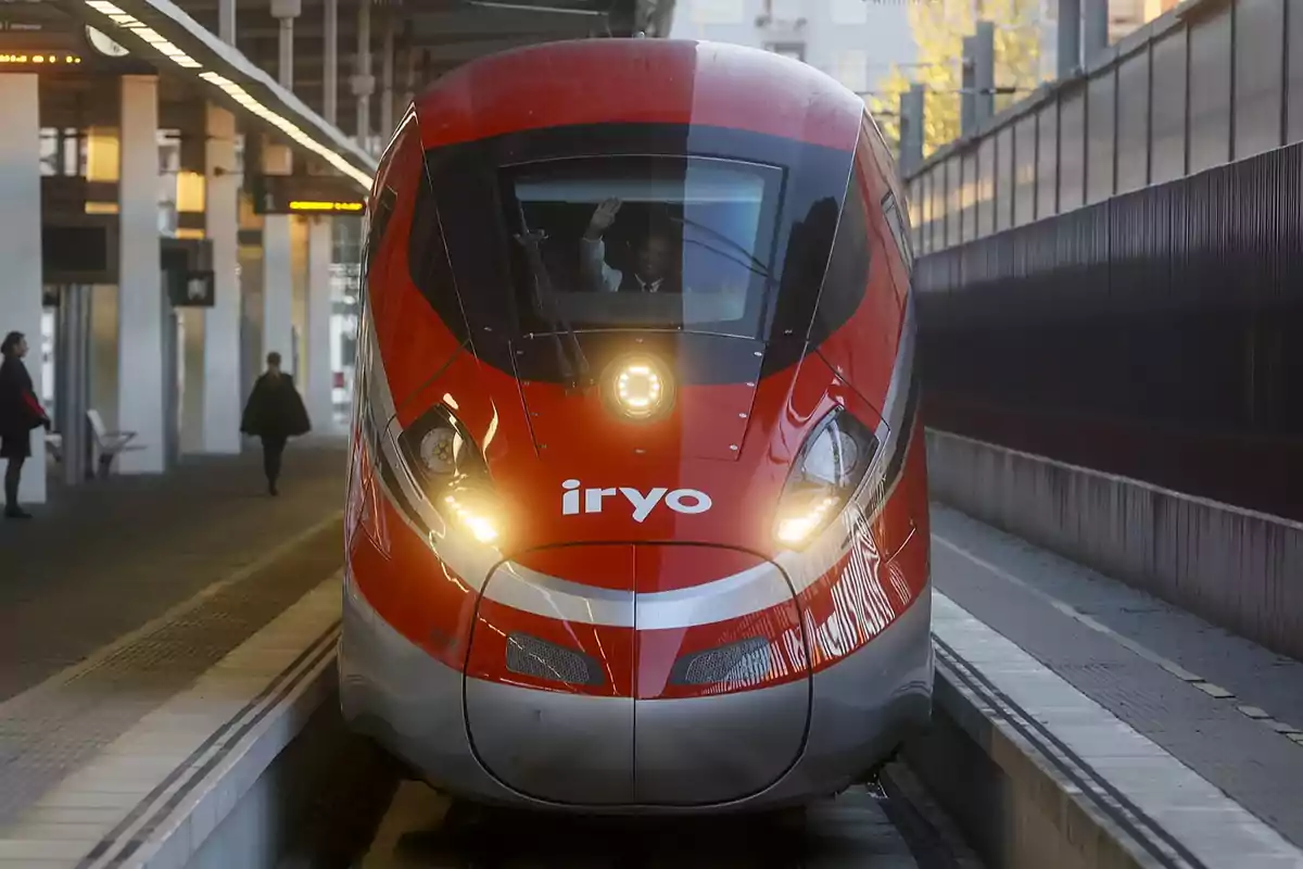 Tren de alta velocidad rojo de la compañía iryo detenido en una estación con personas en el andén Tren de alta velocidad rojo de la compañía iryo detenido en una estación con personas en el andén