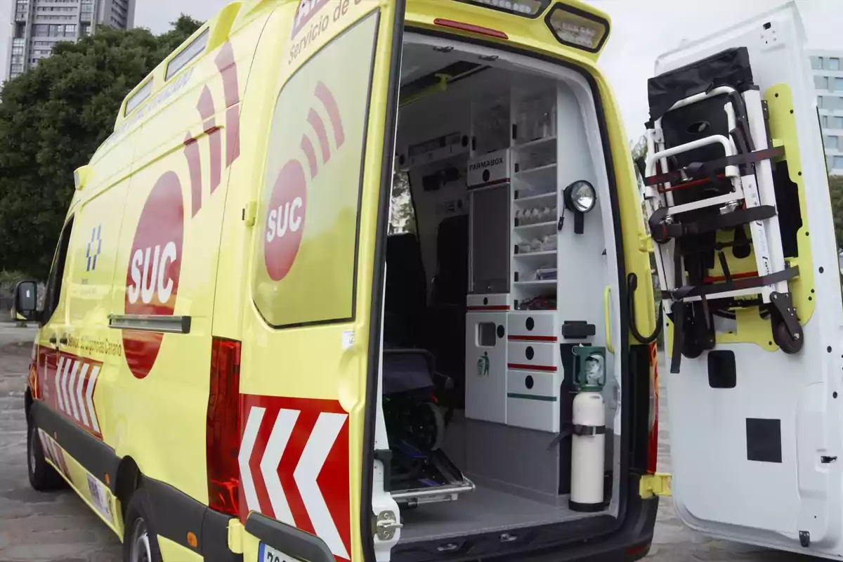 Ambulancia amarilla con las puertas traseras abiertas mostrando el interior equipado con suministros médicos y una silla de ruedas plegable sujeta en la puerta