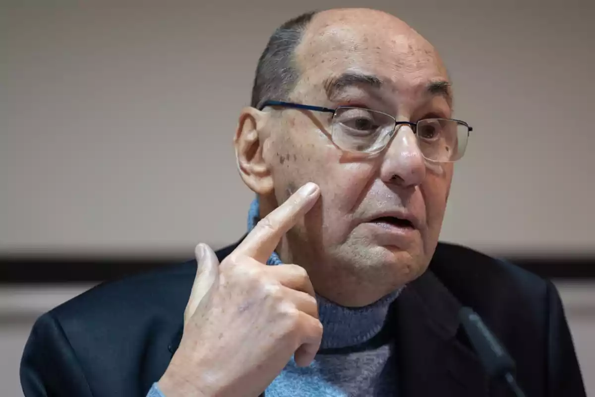 Hombre mayor con gafas señalando su mejilla mientras habla Hombre mayor con gafas señalando su mejilla mientras habla