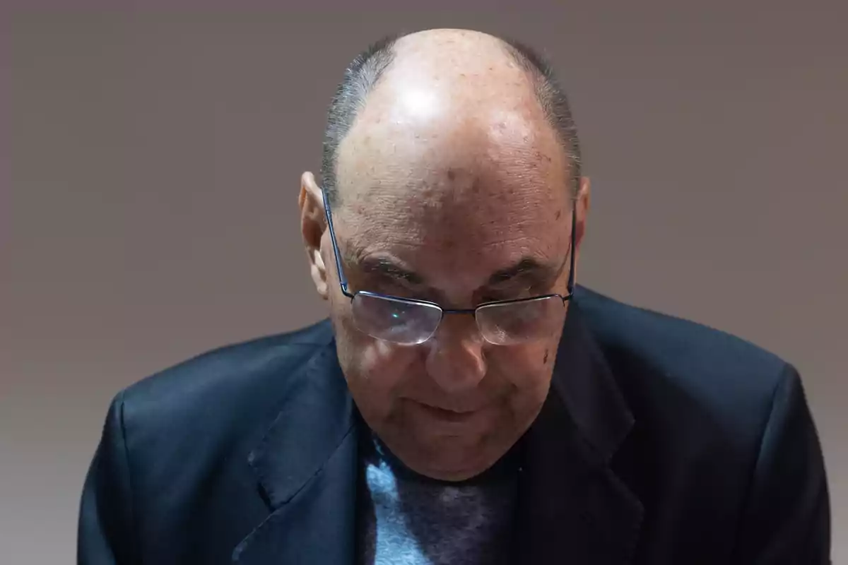 Hombre calvo con gafas mirando hacia abajo vestido con saco oscuro y suéter gris Hombre calvo con gafas mirando hacia abajo vestido con saco oscuro y suéter gris