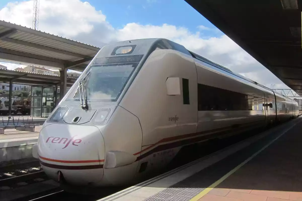 Tren moderno de Renfe detenido en una estación bajo un cielo parcialmente nublado