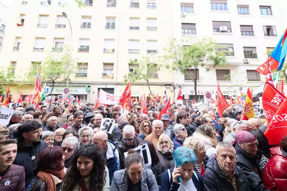 Multitud de personas participando en una manifestación en la calle con pancartas y banderas rojas del PSOE y otras organizaciones frente a edificios residenciales Multitud de personas participando en una manifestación en la calle con pancartas y banderas rojas del PSOE y otras organizaciones frente a edificios residenciales