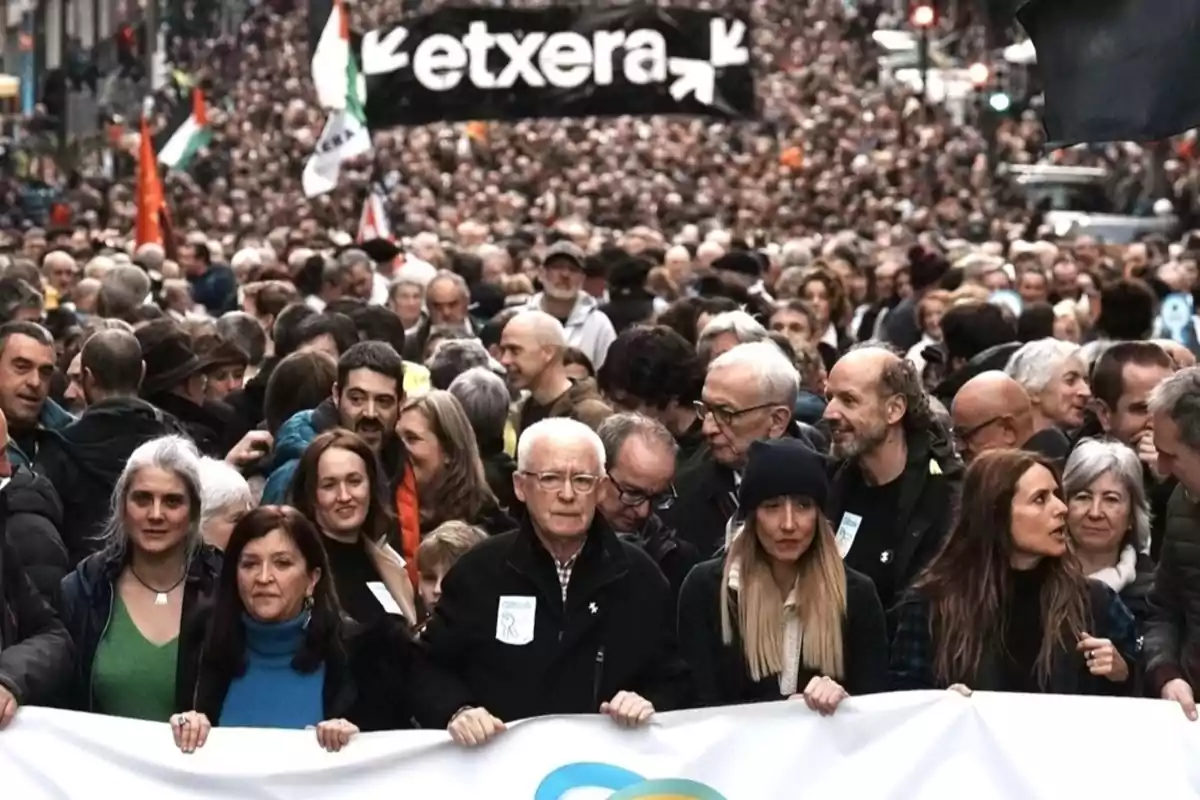 Multitud de personas marchando por una calle con una pancarta al frente y un cartel negro con la palabra etxera al fondo Multitud de personas marchando por una calle con una pancarta al frente y un cartel negro con la palabra etxera al fondo