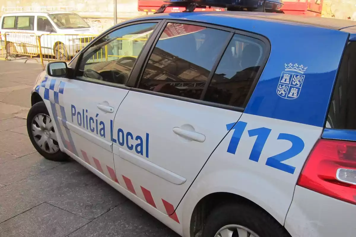 Coche de la Policía Local estacionado en la calle con el número de emergencia 112 visible en la puerta trasera