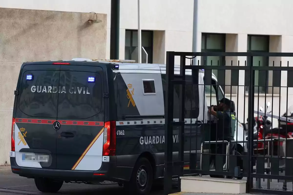 Furgón de la Guardia Civil estacionado junto a una reja con un agente de pie al lado del vehículo