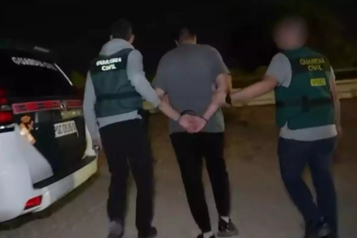 Dos agentes de la Guardia Civil escoltan a una persona esposada junto a un vehículo oficial durante la noche Dos agentes de la Guardia Civil escoltan a una persona esposada junto a un vehículo oficial durante la noche