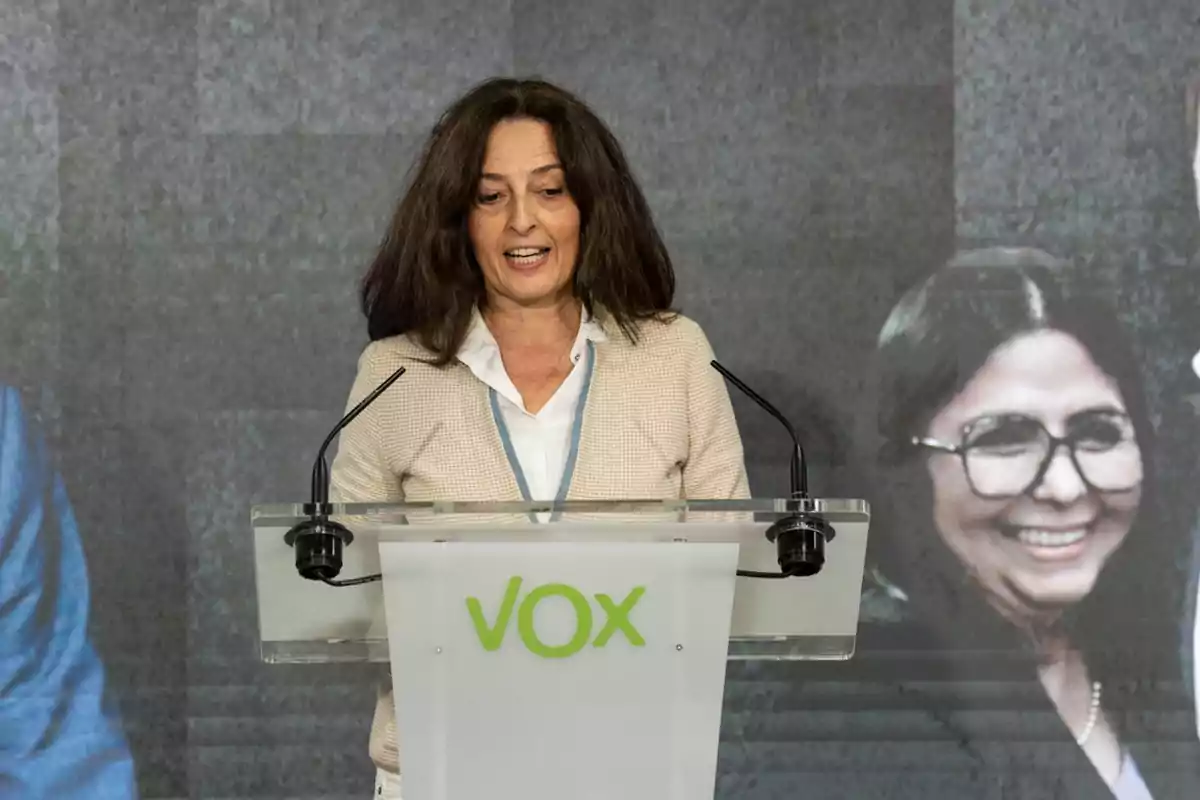 Mujer de cabello castaño hablando en un atril con el logo de VOX al frente y un fondo con imágenes de personas.
