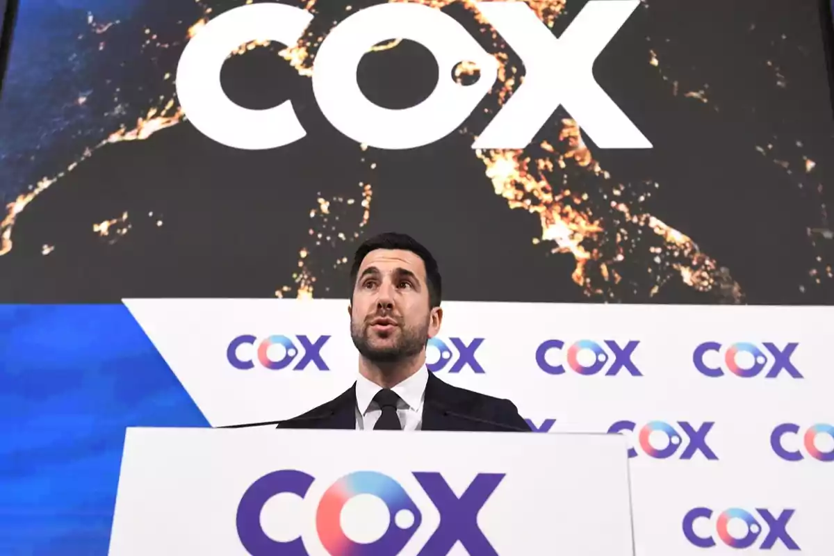 Hombre de traje hablando en un podio con el logo de COX al fondo y en el atril