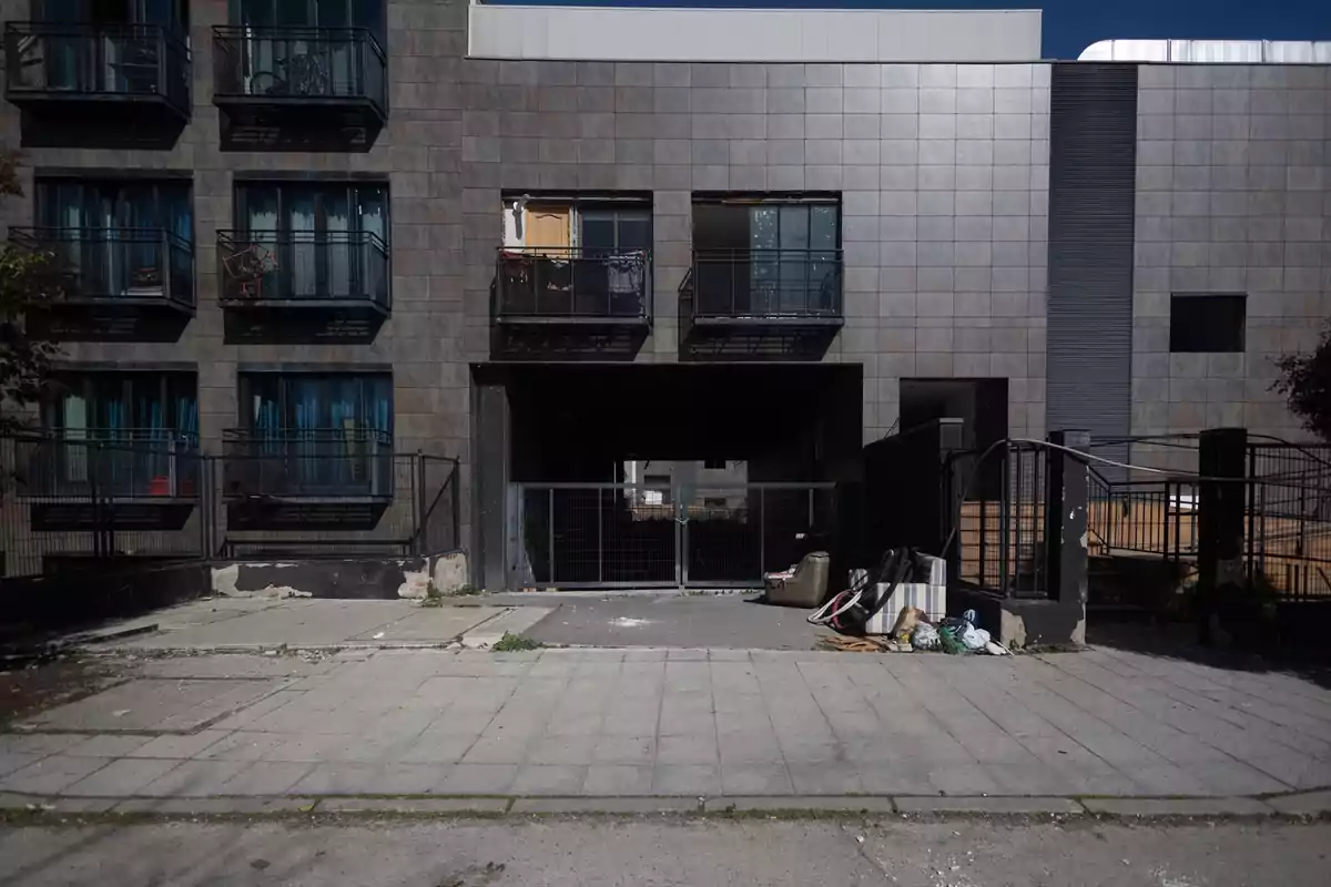 Fachada de un edificio moderno con balcones y ventanas, basura y muebles abandonados en la entrada principal