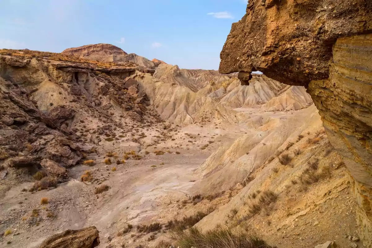 Paisaje árido con formaciones rocosas y colinas de tonos ocres bajo un cielo despejado Paisaje árido con formaciones rocosas y colinas de tonos ocres bajo un cielo despejado