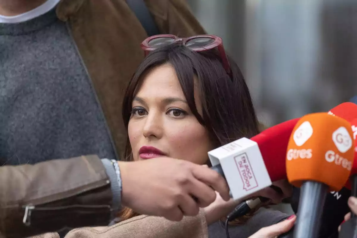 Mujer con gafas en la cabeza rodeada de micrófonos durante una entrevista Mujer con gafas en la cabeza rodeada de micrófonos durante una entrevista