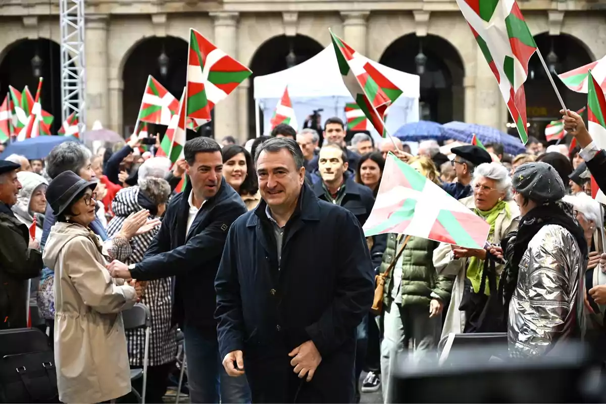 Un grupo de personas sonríe y ondea banderas vascas en una plaza durante un evento público