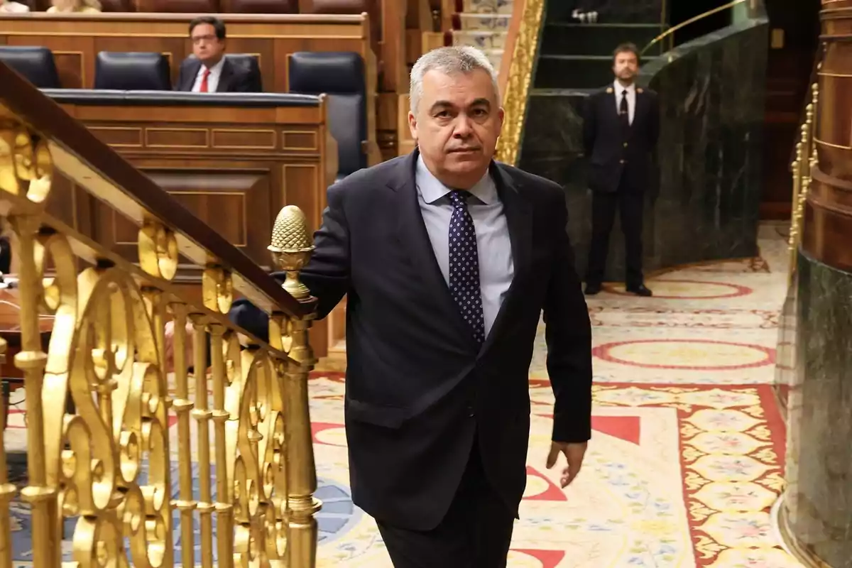 Hombre de traje subiendo una escalera dorada en un recinto parlamentario con alfombra decorada y personas al fondo Hombre de traje subiendo una escalera dorada en un recinto parlamentario con alfombra decorada y personas al fondo
