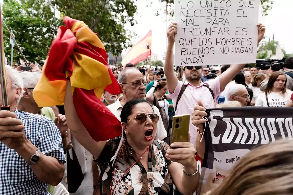 Mujer gritando y sosteniendo una bandera de España en una manifestación rodeada de personas, algunas con pancartas y carteles, en un ambiente de protesta. Mujer gritando y sosteniendo una bandera de España en una manifestación rodeada de personas, algunas con pancartas y carteles, en un ambiente de protesta.