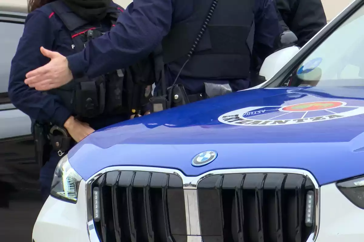 Policías de pie junto a un coche patrulla BMW con el logo de la policía en el capó