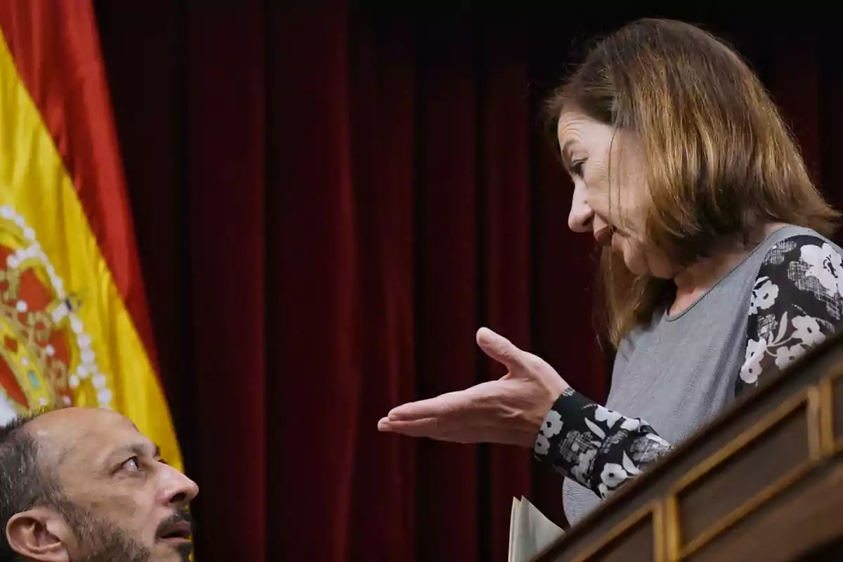 Una mujer y un hombre conversan en un entorno formal con una bandera de España al fondo Una mujer y un hombre conversan en un entorno formal con una bandera de España al fondo