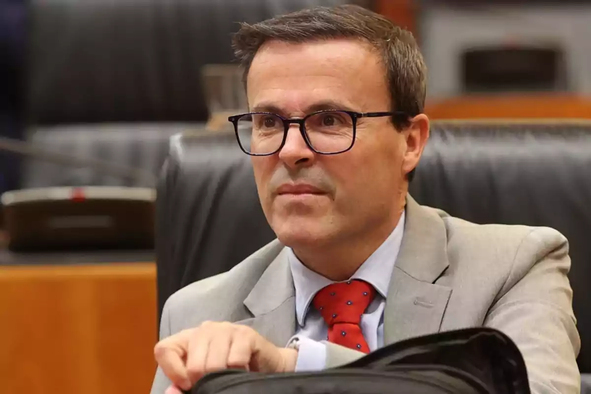 Hombre con gafas y traje gris sentado en una sala de reuniones