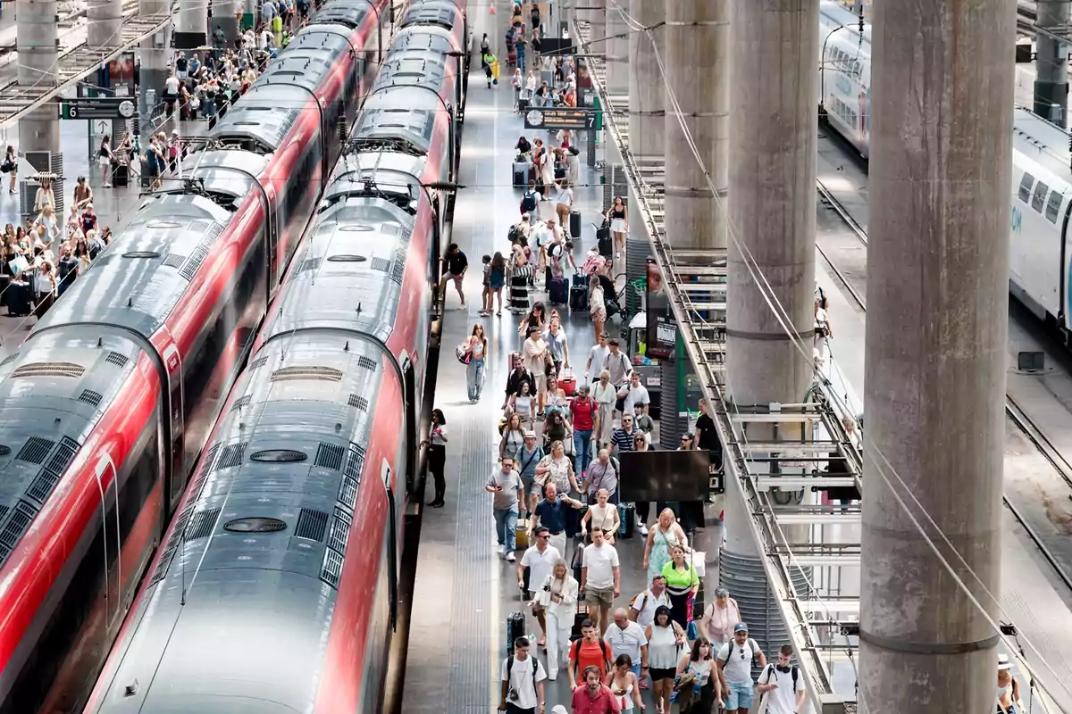 Estación de tren concurrida con muchas personas caminando por el andén junto a trenes rojos y columnas grandes Estación de tren concurrida con muchas personas caminando por el andén junto a trenes rojos y columnas grandes
