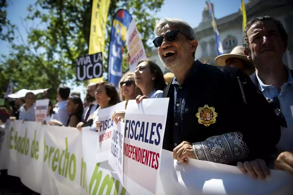 Grupo de personas manifestándose al aire libre sosteniendo pancartas que piden fiscales independientes y muestran mensajes de apoyo a la UCO Grupo de personas manifestándose al aire libre sosteniendo pancartas que piden fiscales independientes y muestran mensajes de apoyo a la UCO