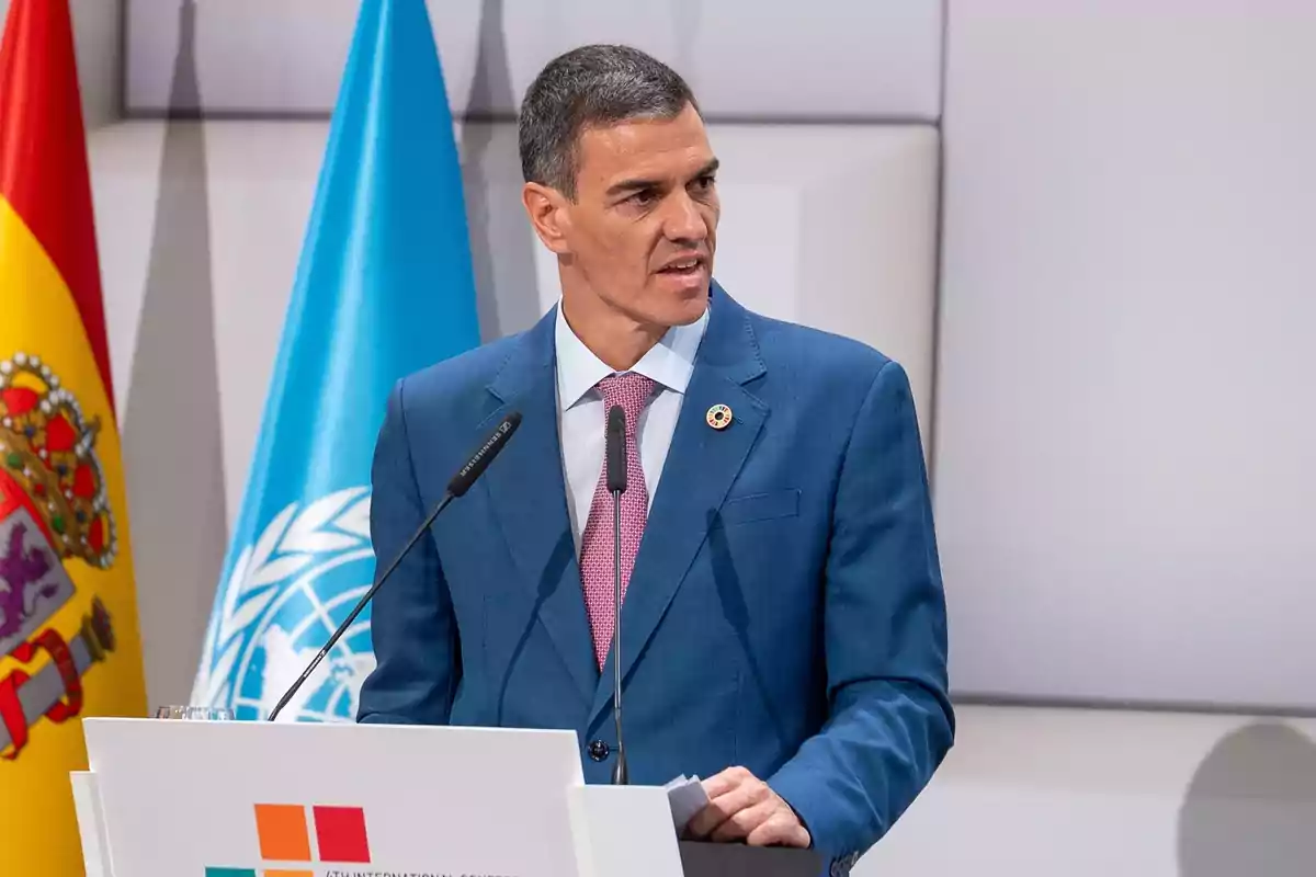 Hombre con traje azul hablando en un podio con las banderas de España y la ONU al fondo Hombre con traje azul hablando en un podio con las banderas de España y la ONU al fondo